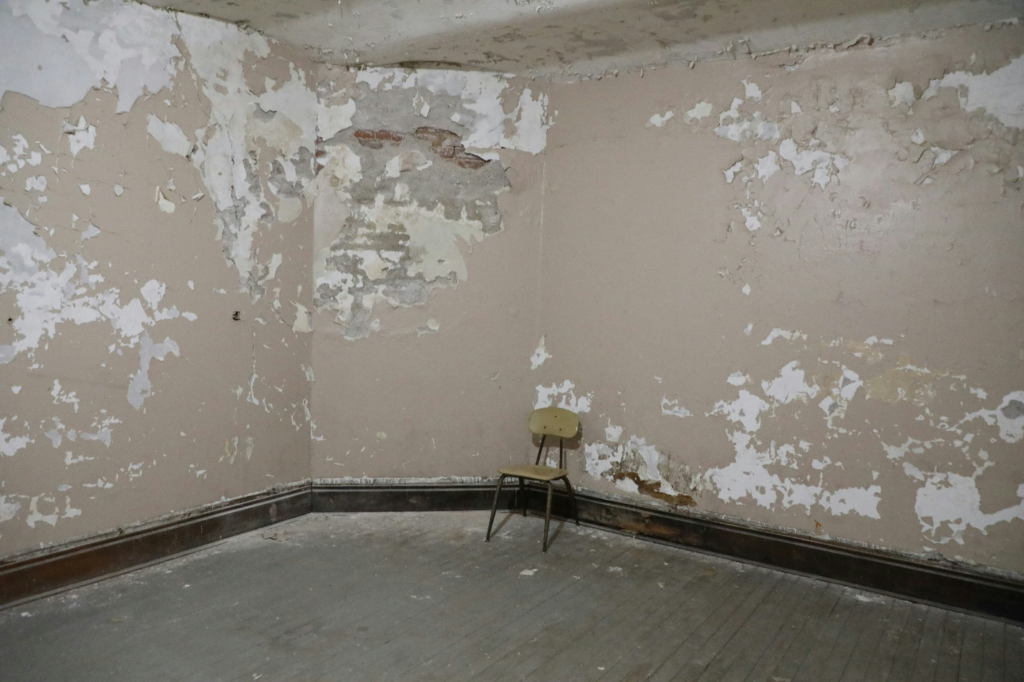 damaged walls of a room with a chair in it.